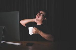 Neck pain or tired concept. Man touching his neck because pain or hurt after long time working on computer in the dark room at home photo