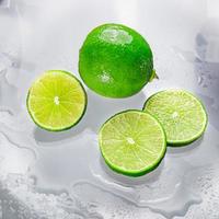 The green lime is blank with the cut lime slice showing the inside of the wet lemon pulp on a clear glass surface, reflecting the shadows of the lime and the wet water, giving it its freshness. photo