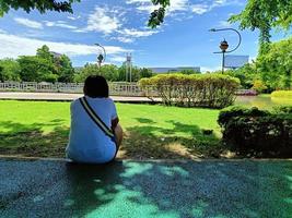 mujer joven deprimida y triste en el suelo en el parque de verano, desde el ángulo posterior foto