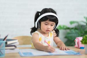 Cute little child wearing white headphone painting with colorful paints. Asian girl using wood color drawing color.Baby artist activity lifestyle concept. photo