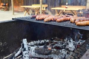 vista superior sabrosas salchichas que chisporrotean en el fuego de la barbacoa a la parrilla en un picnic de verano en una villa rural de vacaciones. comida grasa poco saludable en vacaciones foto