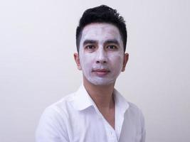 un joven apuesto asiático aplicándose crema en la cara con cara sonriente, concepto de cuidado de la piel foto