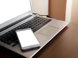 maqueta de pantalla blanca de teléfono inteligente en una computadora portátil maqueta de pantalla blanca de teclado negro en una oficina de escritorio con espacio de copia y composición. el concepto para usar un texto de banner publicitario foto