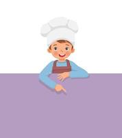 cute little boy in chef hat and apron standing behind empty board pointing finger to blank banner for copy space vector