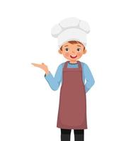 lindo niño con sombrero de chef y delantal con la mano mostrando espacio vacío para copiar vector