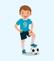 retrato de un niño lindo con ropa deportiva con una pelota de fútbol posando con la mano en la cintura vector