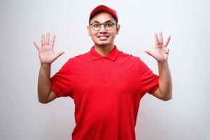 mensajero asiático con uniforme de entrega y gorra mostrando y señalando con los dedos número diez mientras sonríe confiado foto