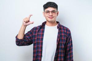 Young handsome man standing smiling and confident gesturing with hand doing small size sign with fingers looking and the camera. measure concept. photo