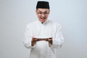 Asian muslim man showing excited expression while holding empty dinner plate photo