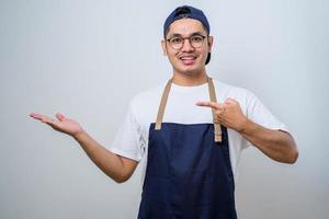 Young handsome asian barista man wearing apron showing product, pointing at something with hands. photo