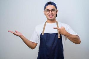 joven y apuesto barista asiático con delantal que muestra el producto, señalando algo con las manos. foto