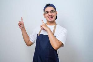 Young handsome barista man wearing apron standing with a big smile on face, pointing with hand and finger to the side looking at the camera. photo