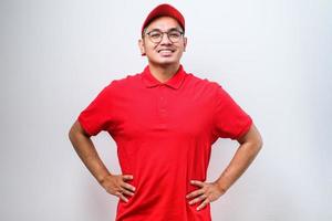 Close-up of confident smiling asian male courier in red uniform and cap, smiling determined, hand on hip photo