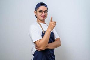 Young handsome asian barista man wearing apron smiling, pointing at something with finger looking at the camera photo
