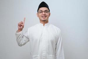 Asian muslim man raising a finger got a good idea looks surprised with a smile photo
