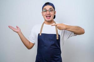 Young handsome asian barista man wearing apron showing product, pointing at something with hands. photo