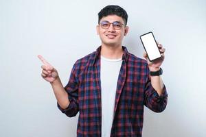 joven y apuesto hombre asiático que muestra una pantalla en blanco de un teléfono inteligente muy feliz señalando con la mano y el dedo hacia un lado foto