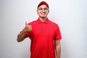 Asian delivery man in red uniform and cap smiling and showing thumb up isolated photo