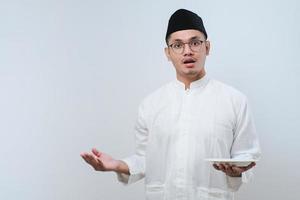 Asian muslim man showing disappointed expression while showing empty dinner plate photo