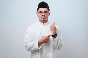 Asian muslim man wearing casual muslim clothes in hurry pointing to watch time, impatience. photo