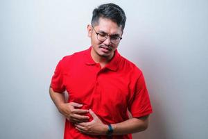 Young handsome Asian man with hand on stomach because nausea, painful disease feeling unwell. Ache concept. photo