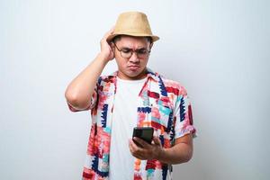 Portrait of unhappy Asian man in casual beach shirt holding mobile phone with sad expression on face while scratching his head. photo