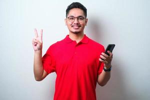 Young handsome Asian wearing casual shirt and glasses holding smartphone and pointing up with fingers number two while smiling confident and happy photo