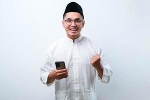 Asian muslim man holding smartphone doing winning gesture holding mobile phone, Happy get special gift online photo