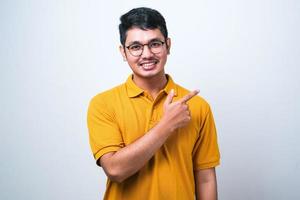 Asian man wearing casual shirt over white background with a big smile on face, pointing with hand finger to the side looking at the camera. photo