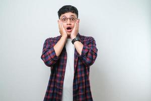 Young handsome Asian man wearing casual shirt and glasse afraid and shocked, surprise and amazed expression with hands on face photo