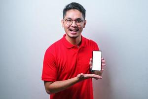 Asian Guy wearing red shirt smile looking to camera showing smartphone empty screen recommending application photo