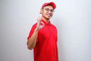 joven repartidor asiático con gorra con una gran sonrisa haciendo el signo correcto, pulgar hacia arriba con los dedos, excelente signo foto