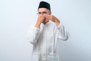 Asian muslim  man wearing glasses over white background smelling something stinky and disgusting photo