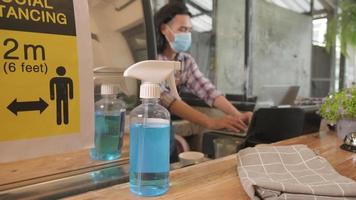 Alcohol sanitizer for healthy protection in a cafe, Asian male barista in face mask use laptop, waiting for coffee order in COVID19 pandemic quarantine, the economic impact for small business startup. video