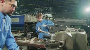 El equipo profesional de la industria, dos trabajadores con uniformes de seguridad y un socio de ingenieros trabajaron con herramientas de metalurgia, tornos mecánicos y talleres de repuestos en la fábrica de fabricación de acero. video