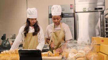 Two female startup chefs live stream via internet online application, demonstrate and show, slice fresh bread with knife in kitchen, pastry cuisine food occupation, social media e-commerce business. video