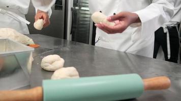 primo piano della mano degli chef in bianco, uniformi da cuoco e grembiuli, stanno impastando pasta cruda, preparando pane, torte, torte e prodotti da forno freschi, cuocendo in forno nella cucina in acciaio inossidabile del ristorante. video