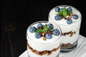 Homemade layered dessert with fresh blueberries, cream cheese or yogurt, granola on rustic background. photo