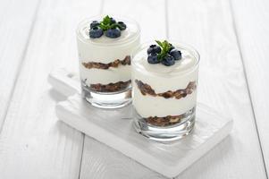 postre con requesón, arándanos frescos y granola en un vaso sobre un fondo blanco de madera. foto