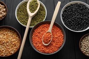 Overhead view of bowls of assorted raw legumes on a dark wooden table photo