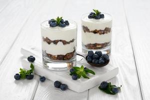 Dessert with cottage cheese, fresh blueberries and granola in a glass on a white wooden background. photo