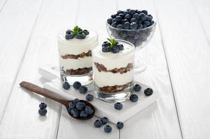 Dessert with cottage cheese, fresh blueberries and granola in a glass on a white wooden background. photo