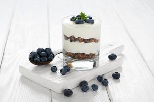 Dessert with cottage cheese, fresh blueberries and granola in a glass on a white wooden background. photo
