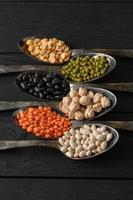 Variety of legumes in old silver spoons on a black wooden background. photo