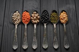Variety of legumes in old silver spoons on a black wooden background. photo