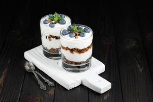 Homemade layered dessert with fresh blueberries, cream cheese or yogurt, granola on rustic background. photo