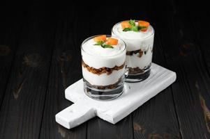 Homemade layered dessert with fresh apricot, cream cheese or yogurt, granola on rustic background. photo