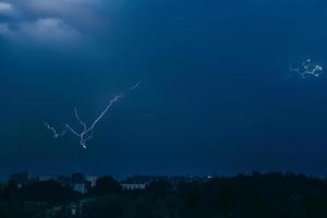 Lightning in sky over city. Bright flashes on dark night. Thunderclouds and electricity discharges in  atmosphere. photo