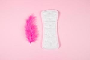 Sanitary pad and pink feather on colored background. Daily feminine hygiene product. photo
