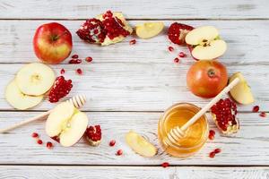 feliz rosh hashaná. símbolos tradicionales de la celebración del año nuevo judío. manzanas, granadas y miel sobre fondo blanco de madera. foto